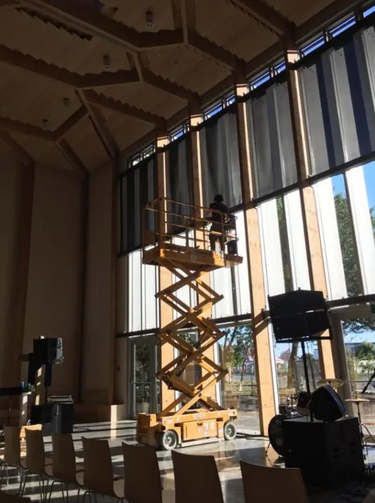 Electrician on a scissor lift in a tall timber-framed hall