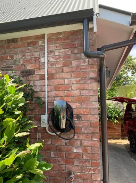 Stainless EV charger mounted on a brick wall beside a driveway