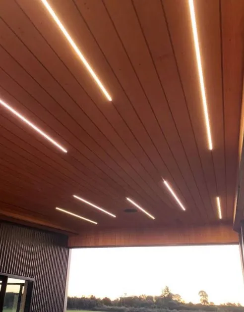 Timber-lined outdoor ceiling with recessed LED strip lights, looking out over a paddock